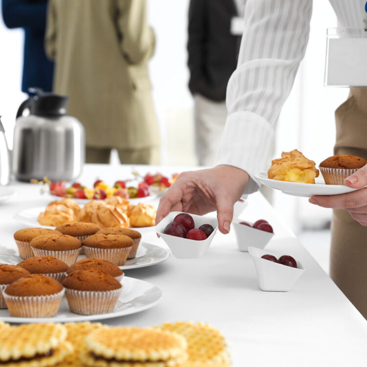 a businessperson holds a plate filled with breakfast treats such as muffins and fruit