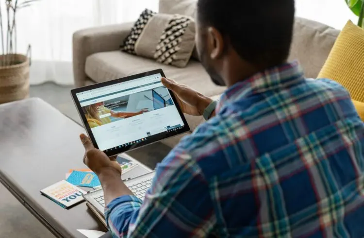 A black man is sat with an ipad looking at LinkedIn Sales Navigator. We are looking over his shoulder as he is sat on a sofa.